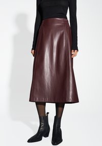 Mittelbrauner Leder-Midrock mit ausgestelltem Design, seitlichen Nähten und glatter Oberfläche. Kombiniert mit schwarzen Stiefeletten.