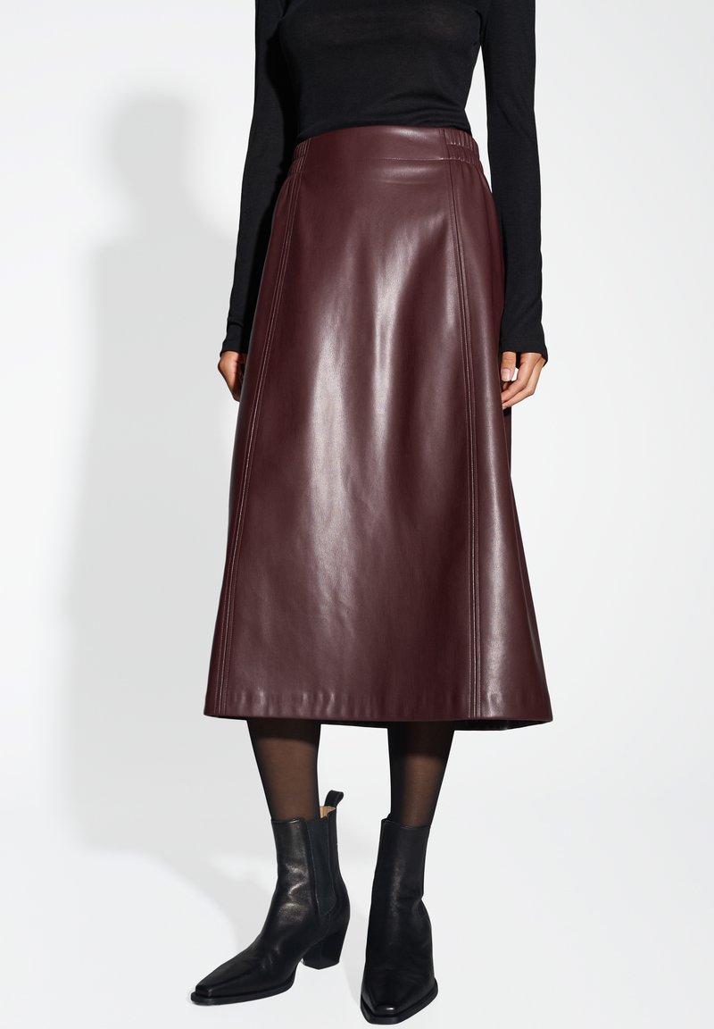 Mittelbrauner Leder-Midrock mit ausgestelltem Design, seitlichen Nähten und glatter Oberfläche. Kombiniert mit schwarzen Stiefeletten.