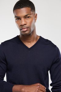 Navyblauer V-Ausschnitt-Pullover mit gerippten Bündchen und Struktur. Schlankes Design, weicher Stoff, minimale Details, getragen über einem unbedeckten Hautton.