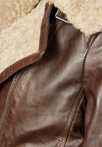 Veste en cuir marron avec un col beige duveteux. Dotée d'une fermeture éclair, d'une texture lisse et de détails de couture visibles.