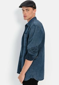 Blauw gestreept shirt in een relaxte pasvorm, met een button-down kraag en lange mouwen. Zwarte pet met een klein merklabel en een afgeronde zoom.