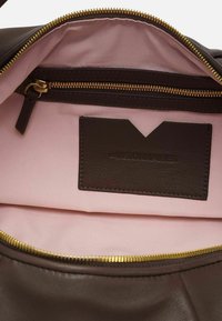 Interno di una borsa a mano in pelle marrone, con una morbida fodera in tessuto rosa, una tasca con zip e un'etichetta marrone scuro con testo in rilievo.