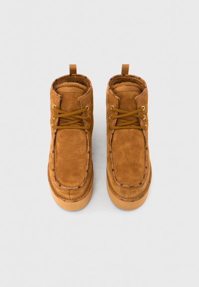 Bottines en daim marron avec bout arrondi, coutures contrastées, fermeture à lacets et doublure douce avec une boucle à l'arrière pour un enfilage facile.