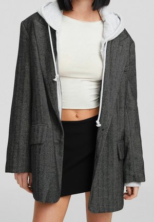 Grå hørgarn oversized blazer med en kontrastfarvet grå hættetrøje under. Kort top og sort nederdel synlig.