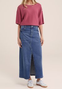 Rosa ribbad kortärmad topp, blå denim maxikjol med en frontslits, och vita sneakers med grå detaljer. Avslappnad outfit mot en ljus bakgrund.