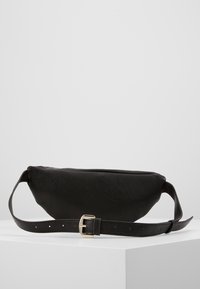 Czarna skórzana nerka o fakturowanej powierzchni, z zamknięciem na zamek błyskawiczny oraz regulowanym paskiem z metalową klamrą. Prosty, elegancki design.