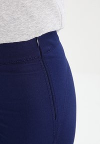 Pantaloni attillati blu navy con una texture liscia, una cerniera laterale e una vita sagomata per una silhouette elegante.