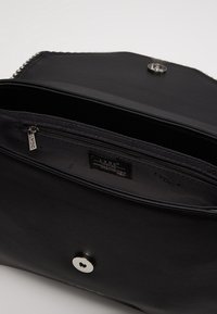 Interno di una borsa a tracolla in pelle nera con scomparto con zip, hardware argentato e etichetta del marchio. Texture liscia, forma rettangolare, chiusura a scatto.