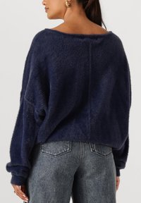 Navy blauw fuzzy sweater met een brede halslijn, verlaagde schouders en opgerolde mouwen, gecombineerd met hoge taille, grijze spijkerbroeken.