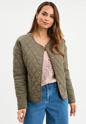 Giacca trapuntata verde oliva con colletto rotondo, chiusura a bottoni automatici e due tasche frontali, abbinata a un maglione multicolore a trama e jeans blu.