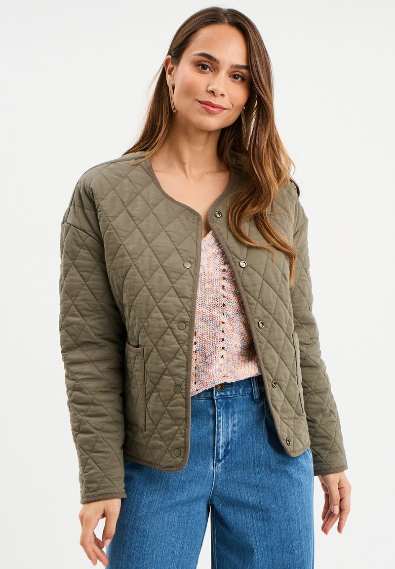 Olivgrüne gesteppte Jacke mit rundem Kragen, Druckknopfverschluss und zwei Vordertaschen, kombiniert mit einem mehrfarbigen strukturierten Pullover und blauen Jeans.