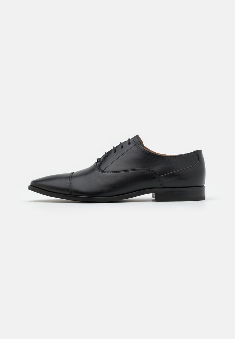 Chaussure Oxford pour homme en cuir noir avec laçage fermé, bout pointu et talon bas sur un fond blanc uni.