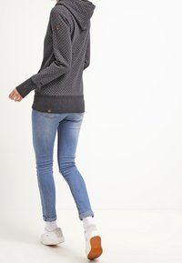 Sudadera gris oscuro con lunares blancos, con capucha, mangas largas y dobladillo acanalado. Combinada con jeans azul claros y zapatos blancos.