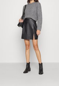 Szary sweter z dzianiny, czarna mini spódnica z teksturą krokodyla i bocznym rozcięciem, zestawiona z czarnymi botkami do kostek i małą czarną torebką na ramię.