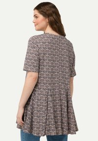 Tunique à motifs violets et beiges avec des manches courtes, un design évasé et un tissu doux. Les détails remarquables comprennent un motif intriqué, semblable à une fleur.