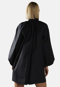 Abito nero oversize con maniche lunghe e gonfiate, scollatura arricciata e dettagli arricciati sulla schiena, realizzato in tessuto testurizzato.