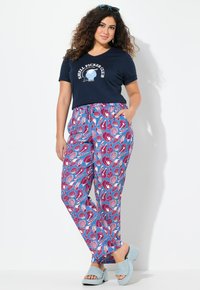 Námořnické tričko s grafikou "Shell Picker Club", v kombinaci s světle modrými kalhotami se živým vzorem mušlí. Světle modré boty na klínu.