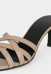 Sandale beige à fines brides et talon haut avec semelle intérieure noire embossée du nom de la marque, dotée d’un talon fin et d’un design à bout ouvert.