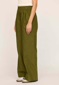 Pantalons larges de couleur vert olive, avec une taille élastique, en tissu léger. Présentent une texture lisse et des détails de couture subtils.