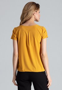 Senfgelbe Bluse mit kurzen Ärmeln in kastiger Form, mit einer Falte im Rücken und hochgerollten Ärmeln, aus einem glatten Stoff gefertigt.