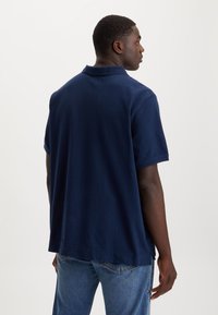 Polo azul marinho em tecido macio com colarinho clássico, mangas curtas e corte descontraído, com fendas laterais na bainha.