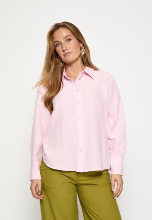 Camisa de botones rosa con mangas largas y cuello, presenta un tejido texturizado, combinada con pantalones verdes anchos.