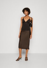 Haut sans manches noir avec un décolleté en V profond, associé à une jupe midi en satin marron. Le modèle porte des sandales à talons noires avec des lanières.