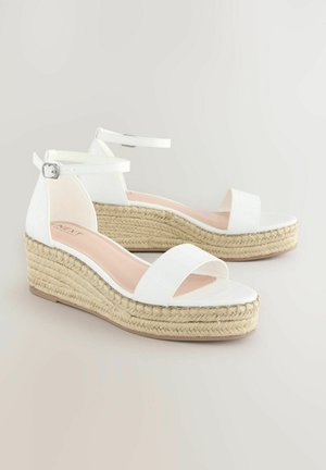 Weiße Wedge-Sandalen mit strukturiertem Finish, offener Zehe und Knöchelriemen. Jute-Plattform und -Sohle. Polsterung sichtbar auf der Innensohle.