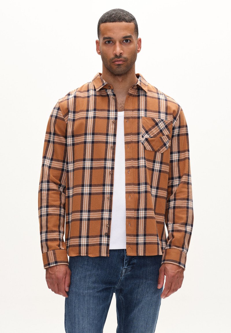 Brunternetternettet flannel skjorte med blå og hvide detaljer, lange ærmer, knaplukning foran og en brystlomme. Parret med en hvid tanktop.