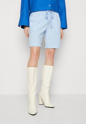 Des shorts décontractés bleu clair avec des revers roulés, une taille à cordon et des poches latérales. Assortis à des bottes à talons blocs blanches montantes.