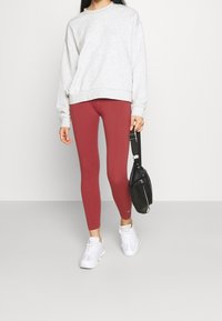 Grå sweatshirt, röda leggings och vita sneakers. Outfitten kompletteras av en liten svart väska med axelrem.