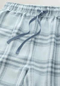 Lyseblå ternede natshorts med et strækbart taljebånd og en blå satin-sløjfe, lavet af blødt stof med en glat tekstur.