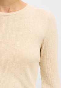 Bézs színű, bordázott hosszú ujjú felső kerek nyakkivágással. Az anyag puha tapintású és finom színárnyalatokkal rendelkezik. Vállnál varrásvonal látható.