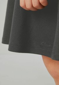 Čierna sukňa vyrobená z hladkej tkaniny, s rovnými okrajmi a šitými detailmi. Logo Clarks diskrétne umiestnené na okraji.