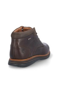 Bota de tobillo de cuero marrón con un acabado suave, acentos marrones contrastantes, puntera redondeada y suela de goma. Presenta costuras sutiles y un detalle del logotipo.