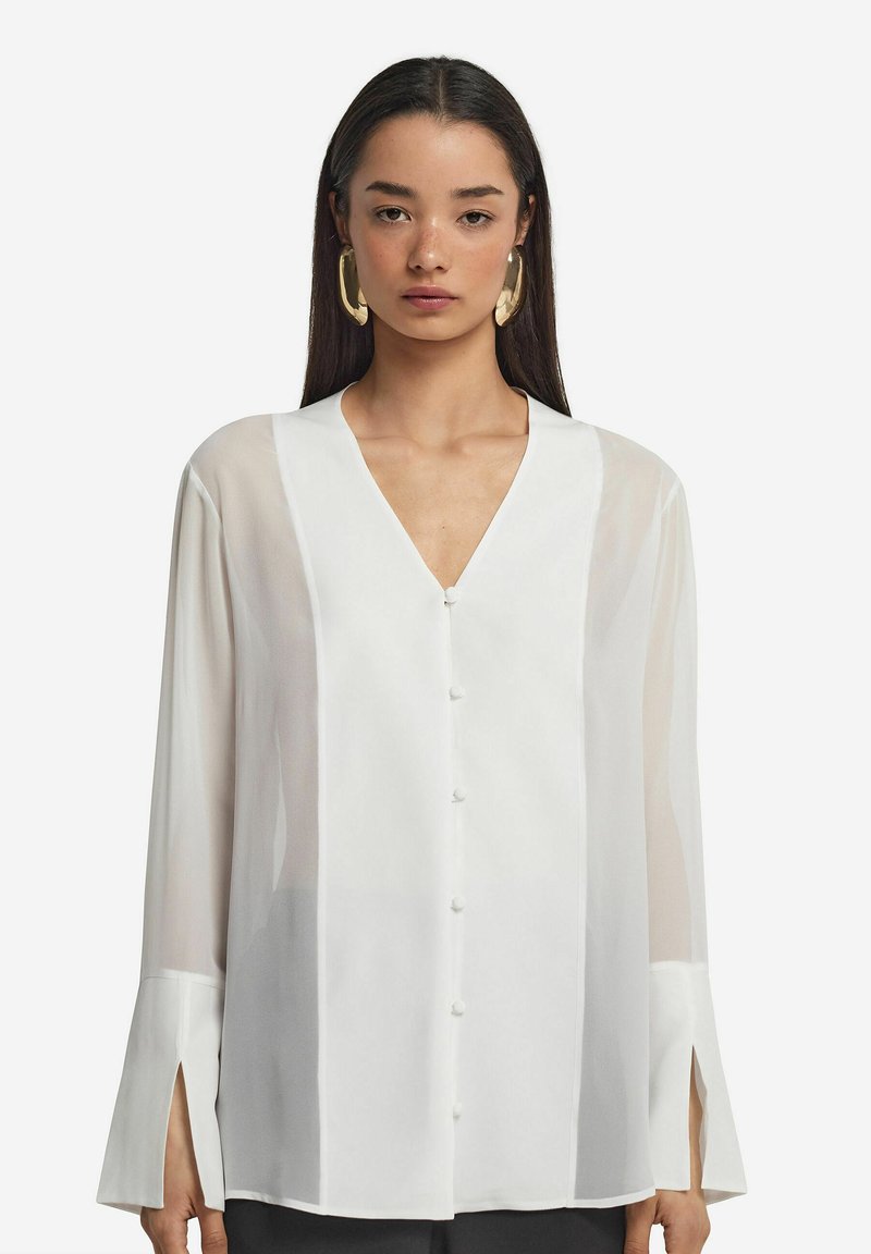 Blusa bianca a maniche lunghe con scollatura a V profonda, bottoni frontali e polsini con spacco; tessuto trasparente con una texture liscia; design minimalista.