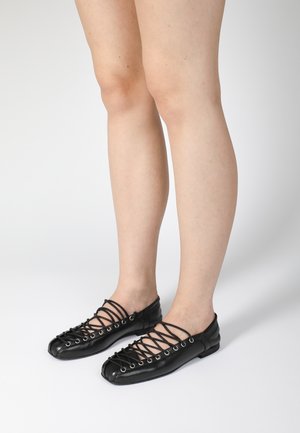 Black leather flat shoes with a pointed toe, featuring crisscross laces and round metallic eyelets. Smooth texture with minimal hardware.