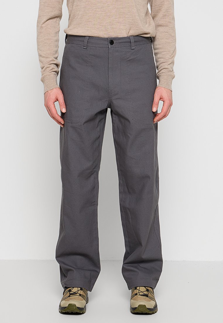 Pantalones de algodón grises con un corte relajado, con cierre de botón y cremallera, dos bolsillos delanteros y combinados con zapatos beige.