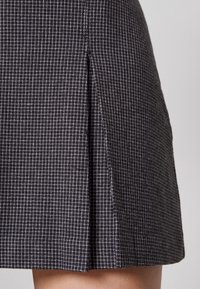 Jupe à carreaux noir et blanc, tissu texturé, longueur genou avec un seul pli sur le côté. Design simple, silhouette cintrée.
