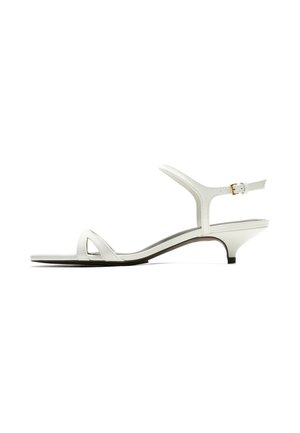 Weißer Kitten-Heel-Sandale mit niedrigem Absatz, dünnem vorderem Riemen, Knöchelriemen und kleiner seitlicher Schnalle, im Profil auf schlichtem Hintergrund gezeigt.