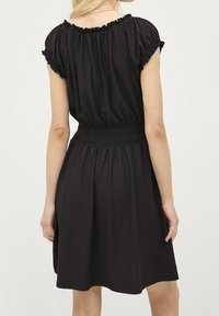 Schwarzes Kleid mit rundem Ausschnitt, kurzen, elastischen Ärmeln, geraffter Taille und fließendem Rock. Weicher Stoff mit glatter Textur.