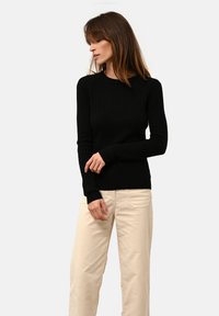 Svart ribbad tröja med långa ärmar och rund hals, parat med ljusbeige vida byxor som visar en figursydd design och texturerad tyg.