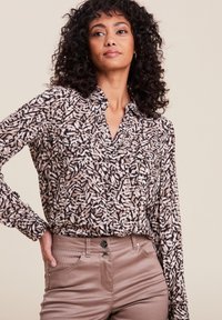 Camicia bottonata con un motivo floreale in sfumature di crema, rosa e nero. Maniche lunghe con una vestibilità comoda e due tasche frontali.