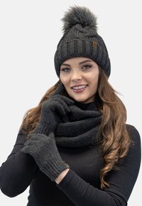 Bonnet en tricot noir avec un pompon en fourrure, gants en tricot noirs assortis et une écharpe texturée, le tout dans différentes nuances de gris foncé.