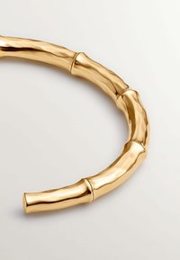 Pulsera en forma de bangle de oro, con una textura lisa y pulida y bordes redondeados, que presenta segmentos distintos que imitan las articulaciones del bambú.