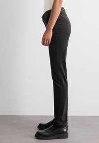 Zwarte denim broek met een slanke pasvorm, voorzien van een middelhoge taille, front pockets en een gladde textuur. Gecombineerd met chunky zwarte loafers.