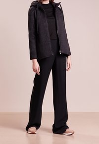 Černá prošívaná bunda s kapucí, zipovým uzavíráním a texturovanou tkaninou, kombinovaná s upnutým černým topem a širokými černými kalhotami.