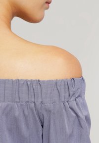 Off-the-shoulder topp i marinblått med vitt rutmönster, med en smockad elastisk halsringning och mjukt, texturerat tyg.