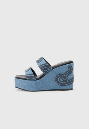 Sandalia de cuña de mezclilla azul con dos tiras estampadas y un diseño curvo en negro y azul en el lateral del tacón plataforma.