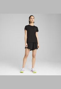 Sort træningsskjorte med korte ærmer, sammen med sorte shorts. Hvide og lilla sneakers med grønne detaljer. Enkel, funktionel design.